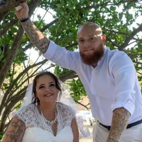 Man and woman in wedding attire standing under a tree